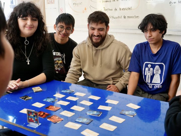 Estudiantes y su profesor alrededor de una mesa con cartas de juego